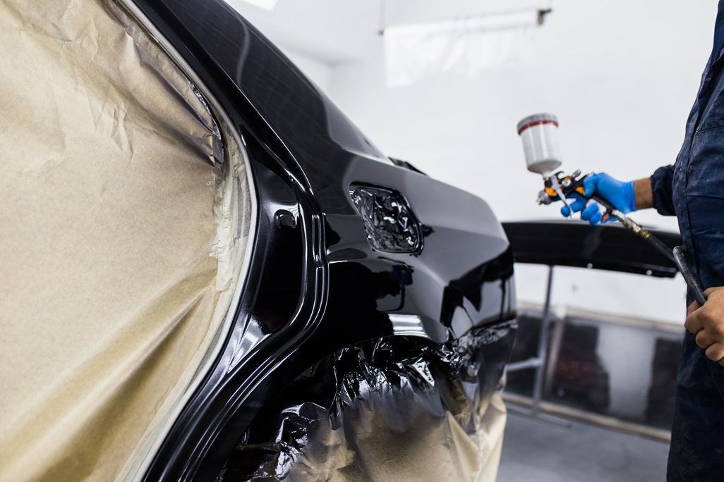 Man with protective clothes and mask painting car using spray compressor. Selective focus.